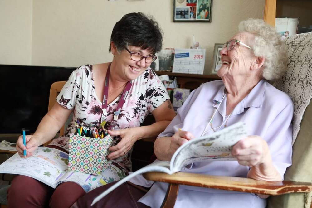 Client and older lady laughing whilst enjoying a colouring activity