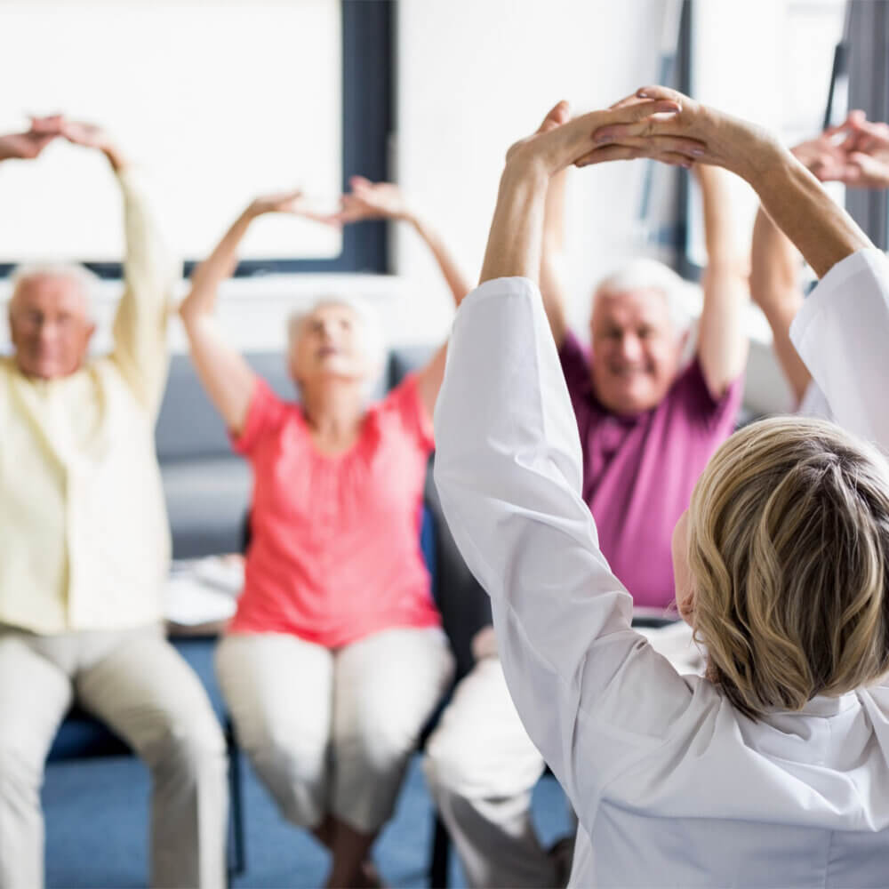 A group of elderly people enjoying a seated yoga exercise class.