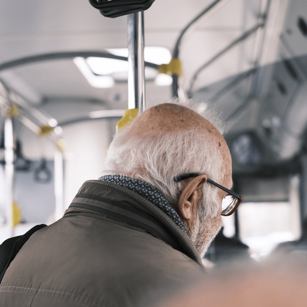 An elderly man standing in the aisle while travelling on a bus