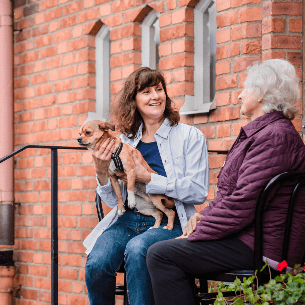 care professional sat chatting to her client outside and holding her dog