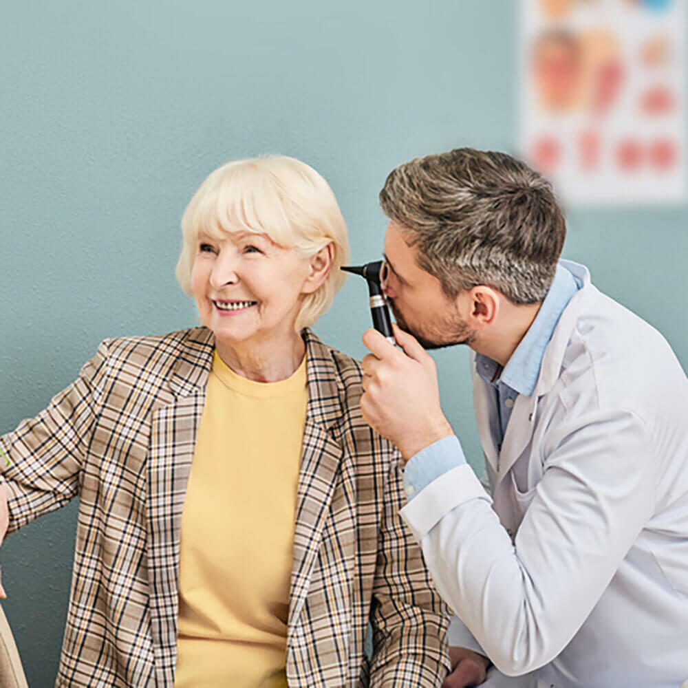 An elderly woman is having her ear examined as part of a hearing test by a doctor.