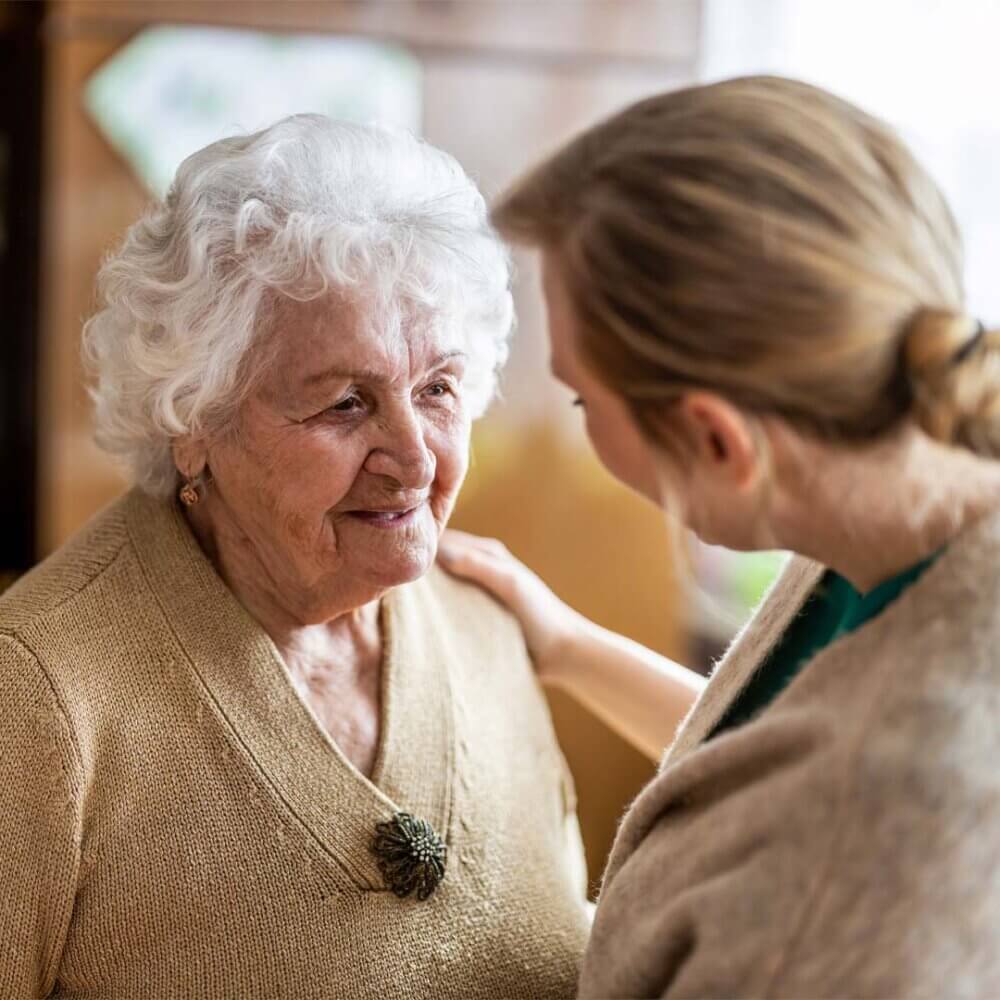 An elderly woman smiling while having a conversation with her daughter.