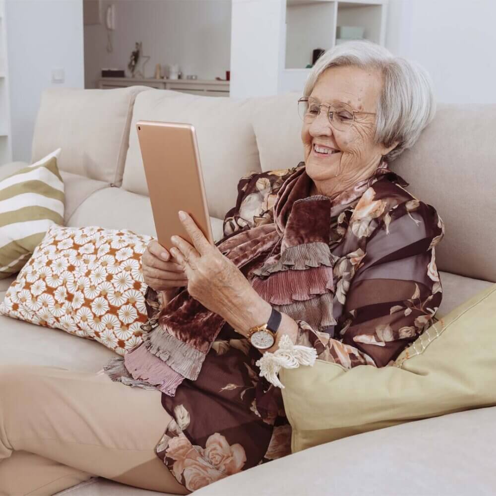 older lady sat on a sofa enjoying time on her ipad
