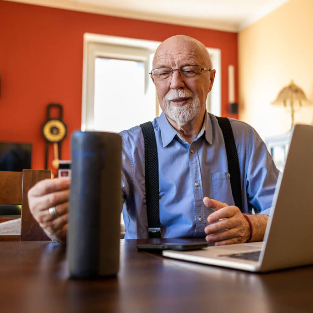 older man sitting at a desk using Alexa smart speaker