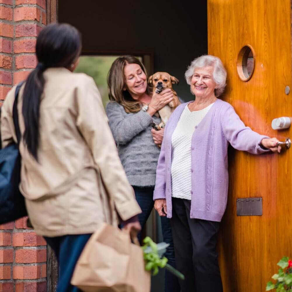 elderly lady and family opening front door to welcome care professional