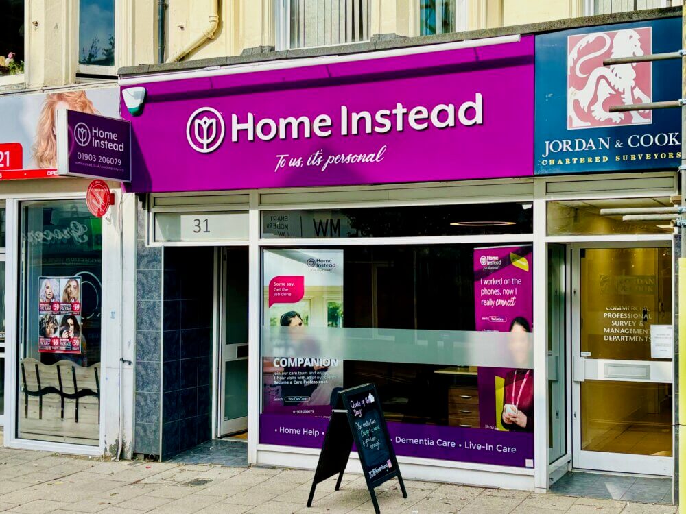 Storefront of "Home Instead," offering services like home help and dementia care, with a purple sign and door poster. - Home Instead